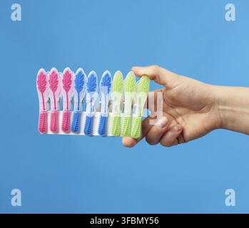 Hand holds a stack of multi-colored plastic clothespins on a blue background Stock Photo