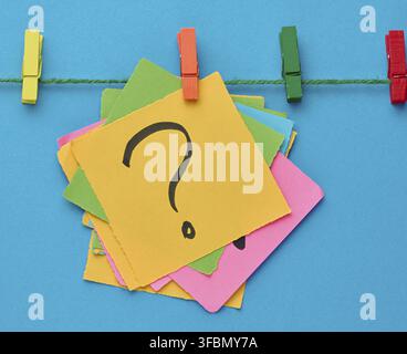 A stack of multi-colored square sticky notes with a question mark on them, attached to a rope with an orange clothespin, a concept of finding a soluti Stock Photo