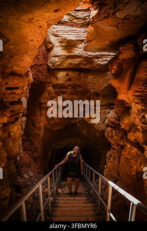 View of a hiker descending a staircase into the French Mountain cave with rugged red rock walls and natural light filtering from above in Antsiranana, Stock Photo
