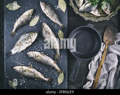 River fish on a black board and a black cast-iron frying pan on a brown table, top view Stock Photo