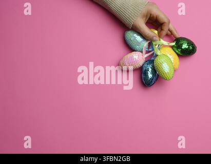 Female hand holding multicolored decorative easter eggs on pink background, copy space Stock Photo