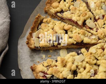 Baked round crumble pie with plum cut into pieces on a black background, close up Stock Photo