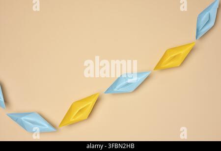 A row of yellow and blue paper boats on a beige background. The paper boats are arranged diagonally Stock Photo