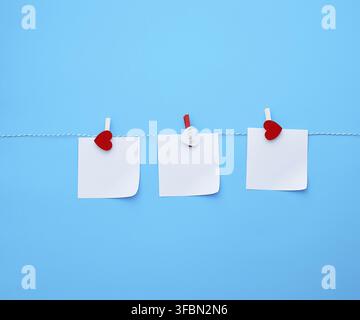 Three empty square white paper sheets hanging on decorative clothespins, blue background Stock Photo