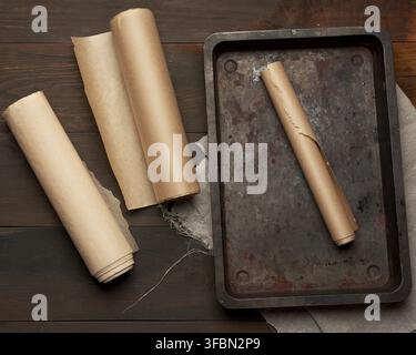 Empty rectangular metal pan and rolls of brown parchment paper on a wooden table, top view Stock Photo