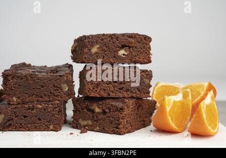 Stack of square baked slices of brownie chocolate cake with walnuts on a white wooden board Stock Photo