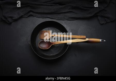 Empty round cast iron frying pan with wooden handle on black table, top view Stock Photo