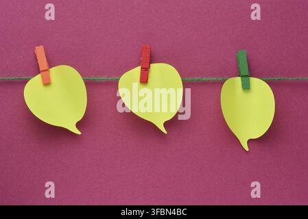 Three yellow thought cloud-shaped sticky notes attached to a rope with multi-colored clothespins on a pink background, concept of task and idea planni Stock Photo