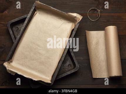 Empty rectangular metal pan covered with brown parchment paper and paper rolls on a wooden table, top view Stock Photo