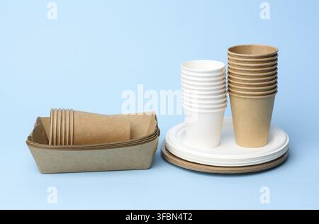 Stack of white and brown paper cups and round plates on a blue background, zero waste Stock Photo
