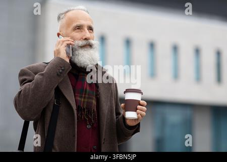 Wealthy senior man with coffee to go having business call Stock Photo