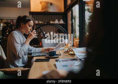 Business professional woman reading documents and drinking coffee in a cozy cafe workspace Stock Photo