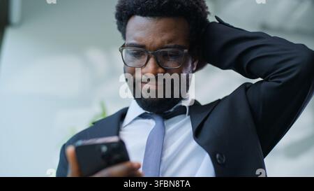 Stressed worried African American business man chatting mobile phone receiving bad news think tired sad ethnic businessman male guy using smartphone Stock Photo