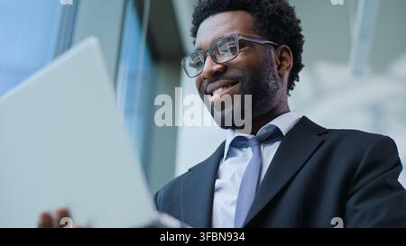 Close up carefree positive African American business man with laptop smiling typing device in office optimistic businessman male guy executive happy Stock Photo