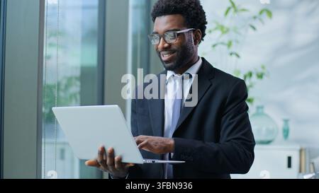Joyful carefree positive African American business man with laptop smiling typing device in office optimistic businessman male guy agent executive Stock Photo