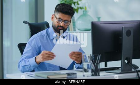 Concentrated Indian business man working typing computer thinking checking documents stats result report in office thoughtful Hindu male executive Stock Photo