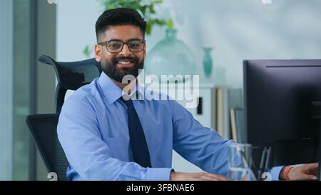 Happy Muslim business man Arabian male typing computer smiling looking at camera in office worker Indian businessman male productive executive Stock Photo