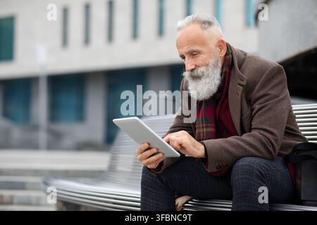 Stylish grey-haired man sitting on the bench, using digital tablet Stock Photo