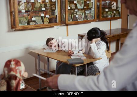 Two young adult female medical students sleeping and looking tired at desk during university lecture. Image represents academic burnout, suitable for higher education marketing Stock Photo