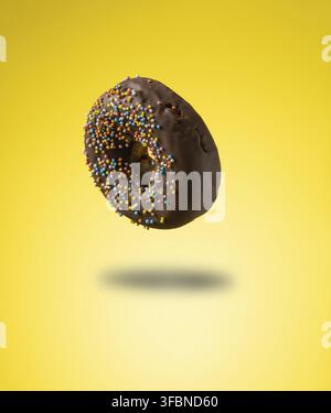 Chocolate donuts with multicolored sprinkles levitate on a yellow background Stock Photo