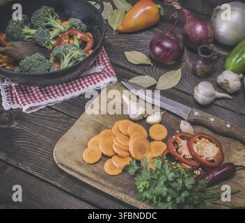 Sliced carrots on a wooden kitchen board and fresh vegetables, top view, vintage toning Stock Photo