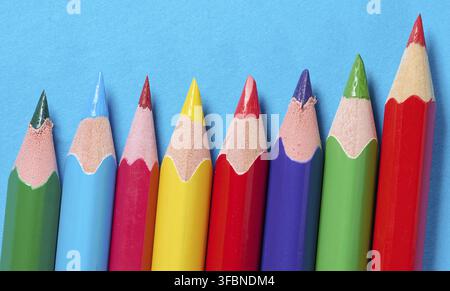 A row of sharpened colored pencils arranged diagonally on a blue background, close-up Stock Photo