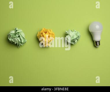 Crumpled colored balls of paper and glass white lamp on green background, top view Stock Photo