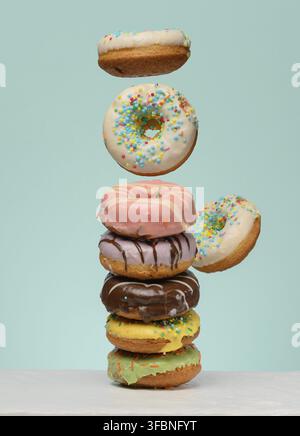 Stack of donuts with various fillings and glazes, several levitating upwards. Blue background Stock Photo