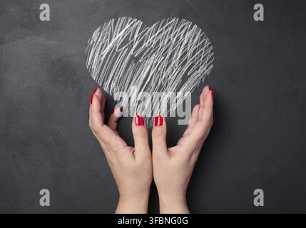 A heart drawn with white chalk on a black board and two female hands Stock Photo