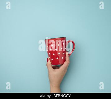 Female hand holding a red ceramic mug on a blue background, break time and drink coffee Stock Photo