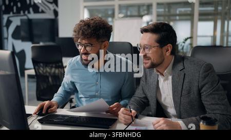 Two multiracial business men analyzing papers review documents charts good result giving high five looking in computer success financial growth Stock Photo