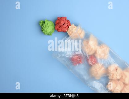Transparent plastic bag with crumpled sheets of paper on blue background, top view Stock Photo