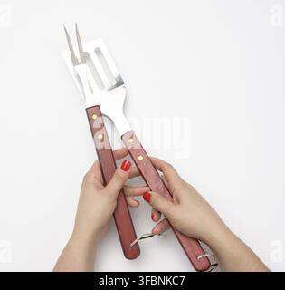Metal spatula with a wooden handle and fork for a picnic in a female hand with painted red nails on a white background Stock Photo