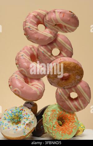 Donuts floating in the air and falling in a chaotic order, covered with pink icing with white stripes. Light beige background Stock Photo