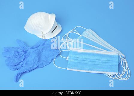 Disposable gloves and stack of medical masks made of non-woven material with white rubber bands on a blue background, protective accessory for the res Stock Photo