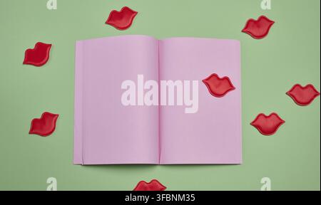 An open notebook with blank pink pages surrounded by red lip appliques on a green background Stock Photo