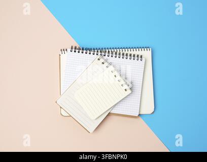 Stack of spiral open notebooks with blank white sheets on a blue background, top view Stock Photo