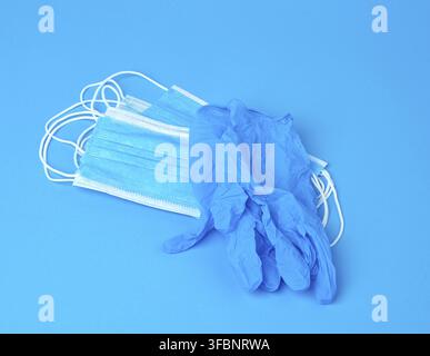 Disposable gloves and stack of medical masks made of non-woven material with white rubber bands on a blue background, protective accessory for the res Stock Photo