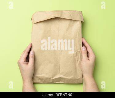 Two hands holding a paper bag of brown kraft paper ona green background, top view Stock Photo