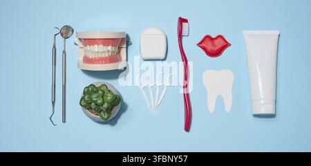Set of oral hygiene products and tools, tube of toothpaste, toothbrush, dental floss, dental instruments, and jaw model on blue background. Top view Stock Photo
