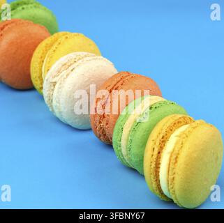 Round multi-colored baked macarons with cream lie in a line on a blue background, close up Stock Photo