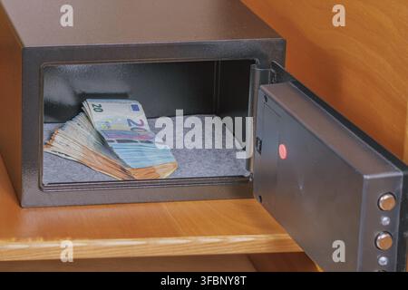 Open small black metal electronic safe box with stack of euro banknotes inside placed on wooden shelf stock photo. Stock Photo
