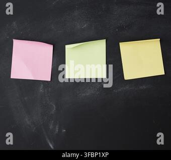 Three blank paper multi-colored square stickers are stuck on a black chalk board Stock Photo