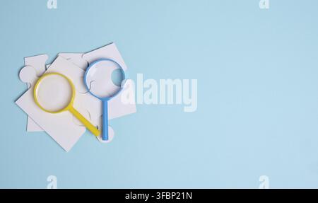 White puzzles and plastic magnifying glass on a blue background, top view Stock Photo