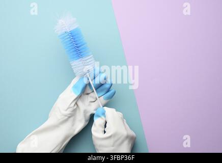 Female hand in white rubber gloves holds a plastic cleaning brush on a blue background, copy space Stock Photo