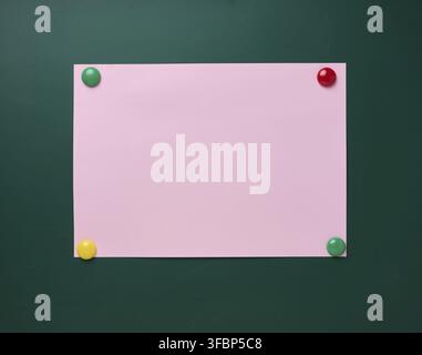 An empty pink paper sheet is attached with magnets to a green school board, a place for an inscription Stock Photo