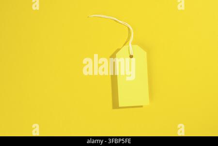 Blank rectangular paper yellow price tag with white rope on yellow background, flat lay Stock Photo