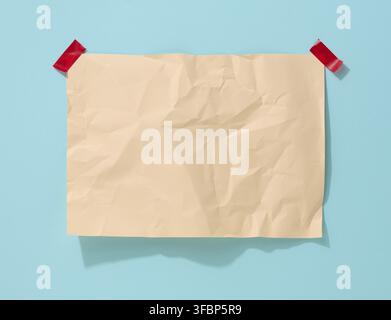 Blank rectangular crumpled beige sheet of paper glued on a light blue background. Place for an inscription, announcement Stock Photo