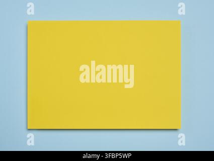 Blank yellow sheet of paper on blue background, abstract backdrop for inscription, copy space Stock Photo