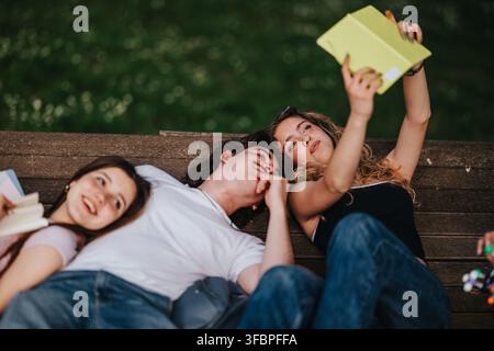 Students relaxing on a park bench taking a selfie while studying with notebooks and books Stock Photo
